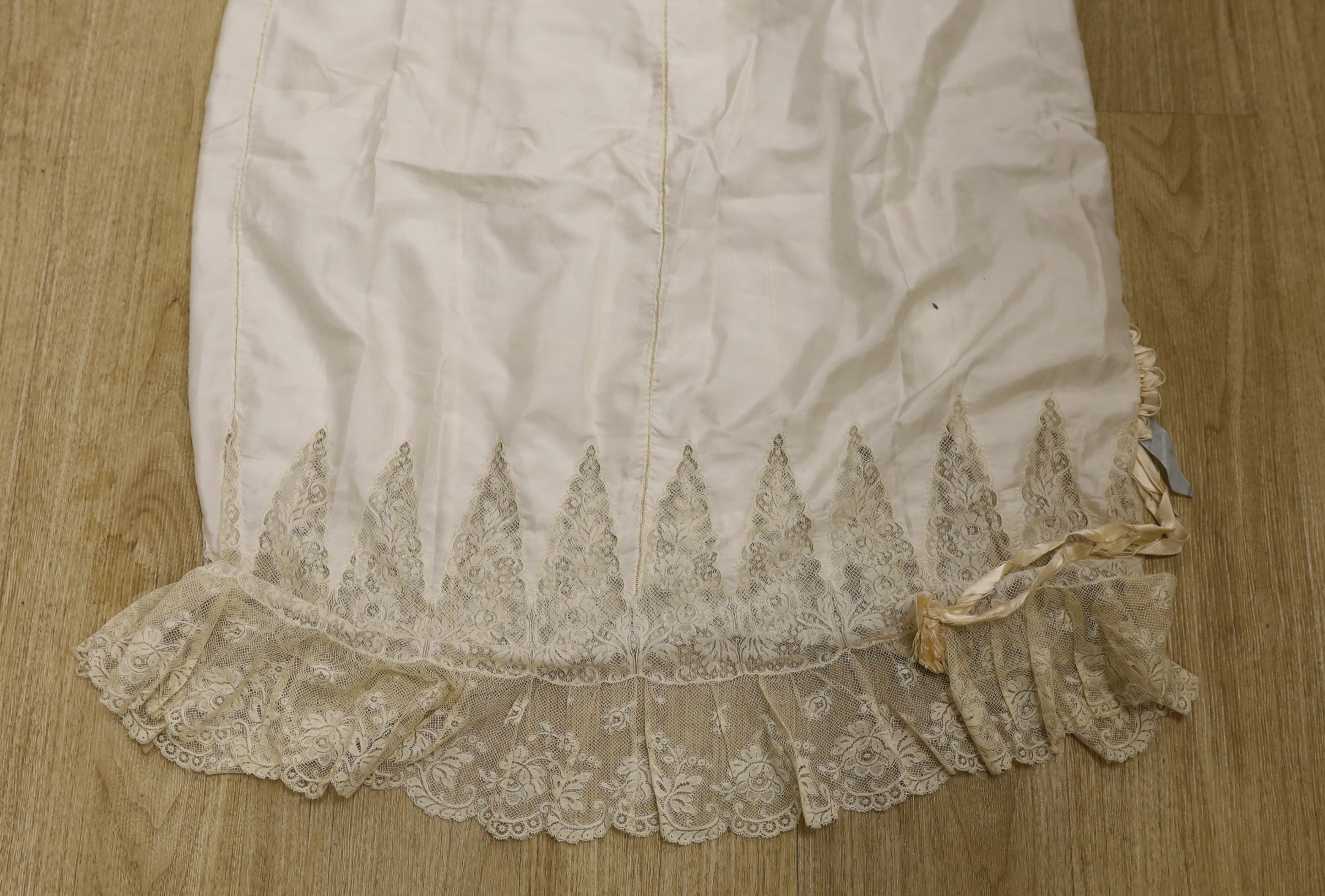 Two 1910-1920 cream silk and lace ladies floor length petticoats, one with a deep border of machine made Valenciennes lace, with a silk and satin ornamental rosette, the other a similar length, with bands of lace and sil